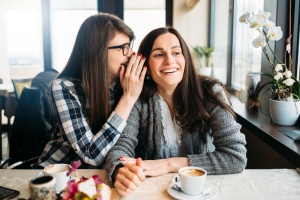 Two smiling friends sharing secret in coffee talk